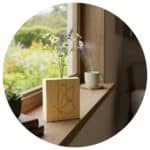 Vlindergravure met vaasje gevuld met wide bloemen op een vensterbank.